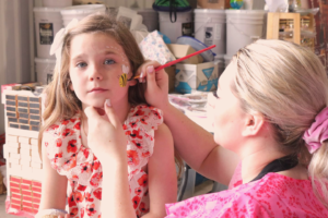 a woman painting a bumblebee on a girl's cheek