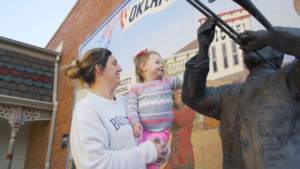 A woman holding a girl next to a statue of a trombone player