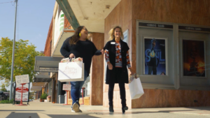 two women with shopping bags walking in front of a movie theater